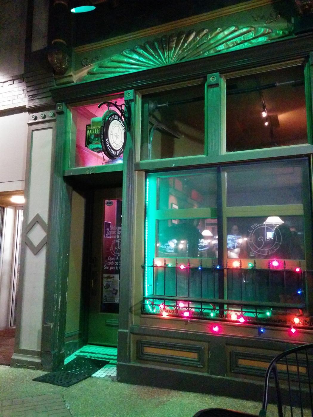 The front of Gumbo Bottoms Ale House at night, a green painted storefront on Madison Street with string lights and a hanging sign